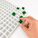 Hand holding an emerald green gummy sample next to the 4mL Square Gummy Mold - 192 Cavities